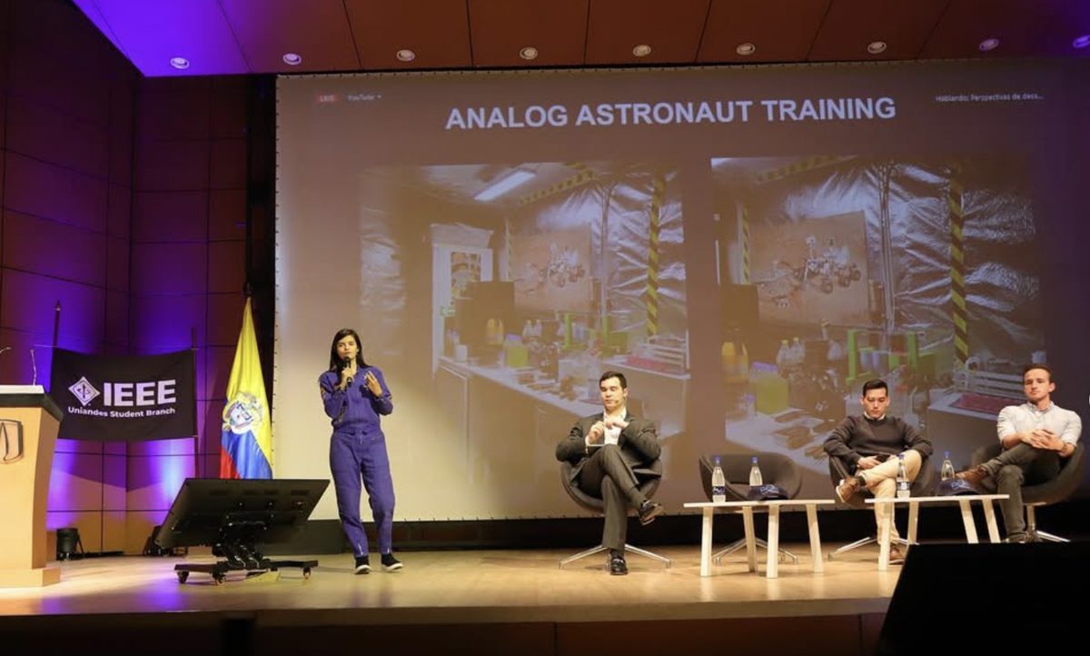 Giovanna Ramírez hablando en el escenario junto a los panelistas, con una diapositiva sobre entrenamiento de astronautas análogos