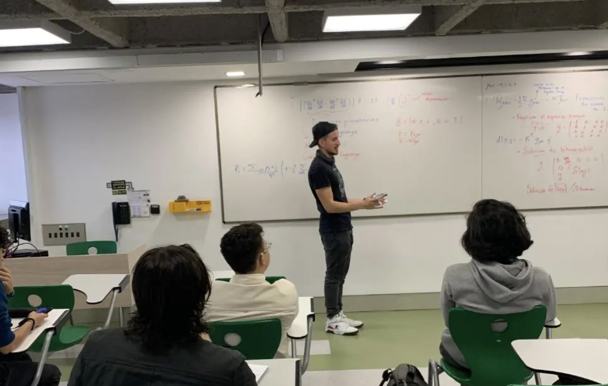 Ponente frente a un tablero con las ecuaciones de campo de Einstein y la solución de Schwarzschild, ante estudiantes en el aula
